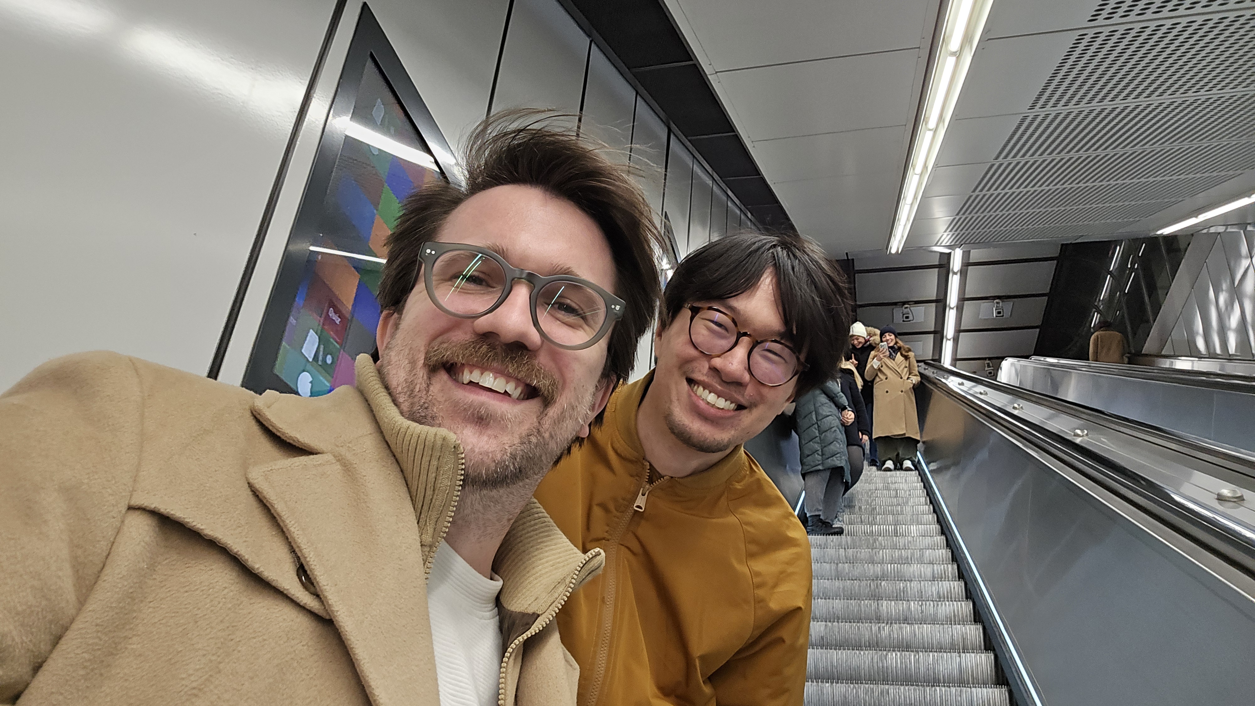 Jonathan Zong and I, smiling and taking a really well framed selfie while on an escalator heading down into a subway station.