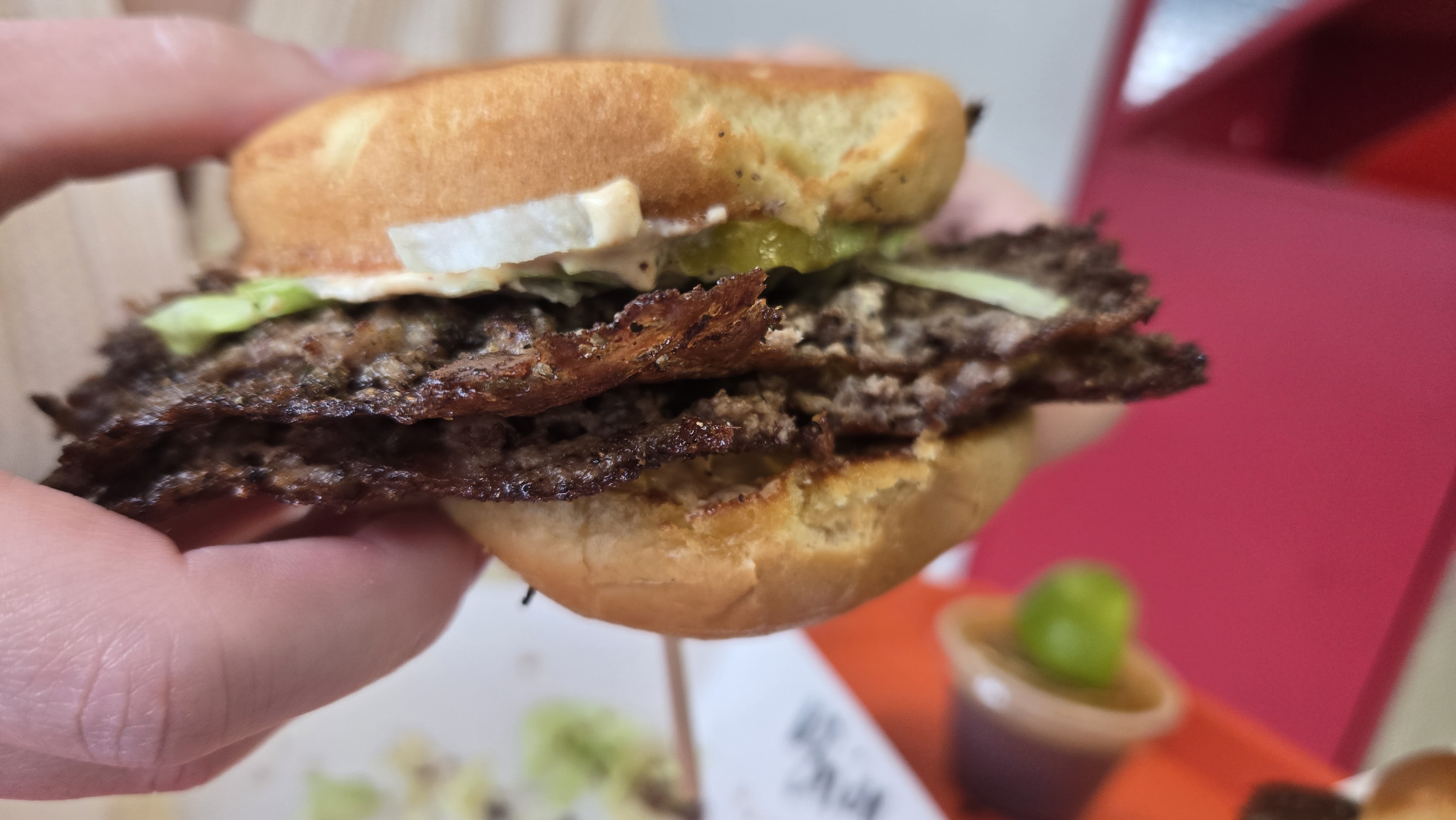 A smash burger viewed from the side and held upside down.