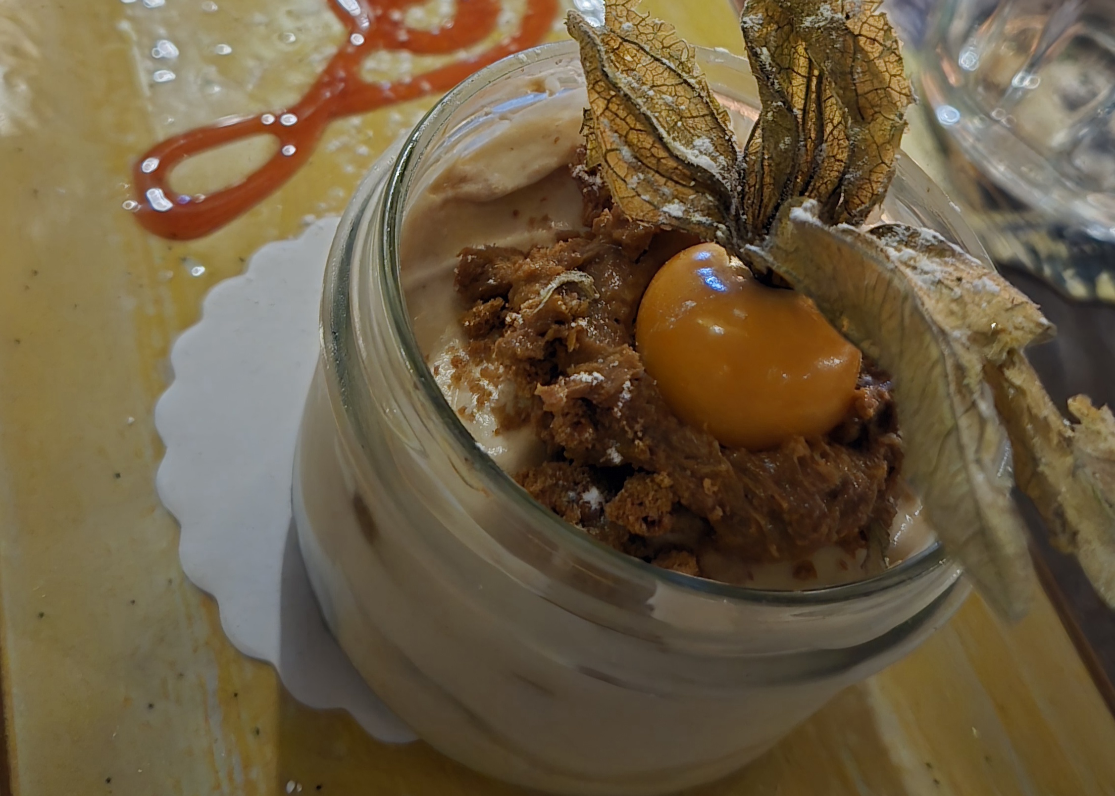 A complicated looking dessert with a small persimmon on top of a fluffy frosting with a brown coloring.